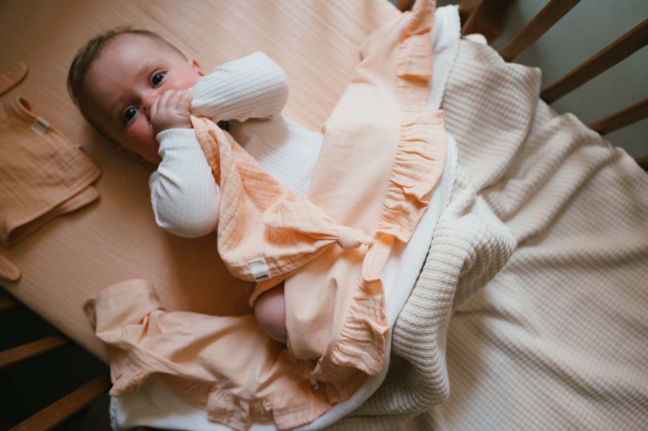 Koeka nieuwe kleur peach bedlinnen van de Faro collectie. In sfeerbeeld van kindje in ledikantje.